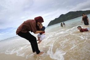5年前在印尼大海啸死里逃生的倖存者尤蕴，已经走出海啸阴影，带著8个月大的儿子在海边戏水。（图：法新社）