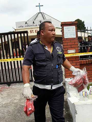 A Kota Tinggi police investigator takes plastics bags that were filled with paint at the St Elizabeth Catholic church in Kota Kecil, Kota Tinggi on Thursday (The Star photo)