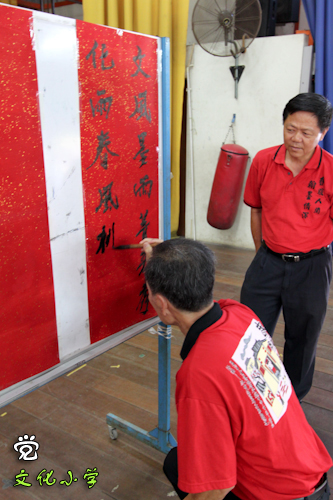 林国安先生在文化小学挥毫，现代书画联盟的会长蔡天成在一旁欣赏。