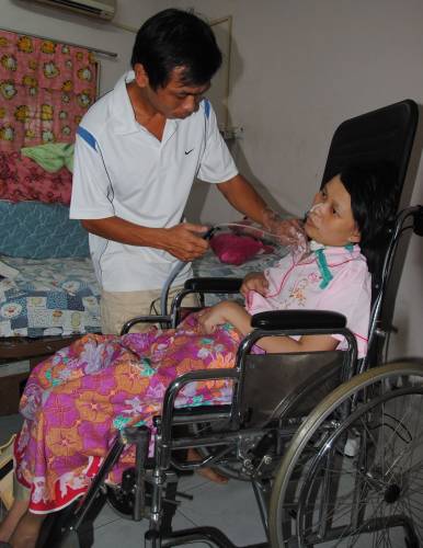 王月芳从昏迷中醒来后变成植物人，丈夫薛顺安（左）在旁细心照顾，每天为她定时抽痰。（图：星洲日报）